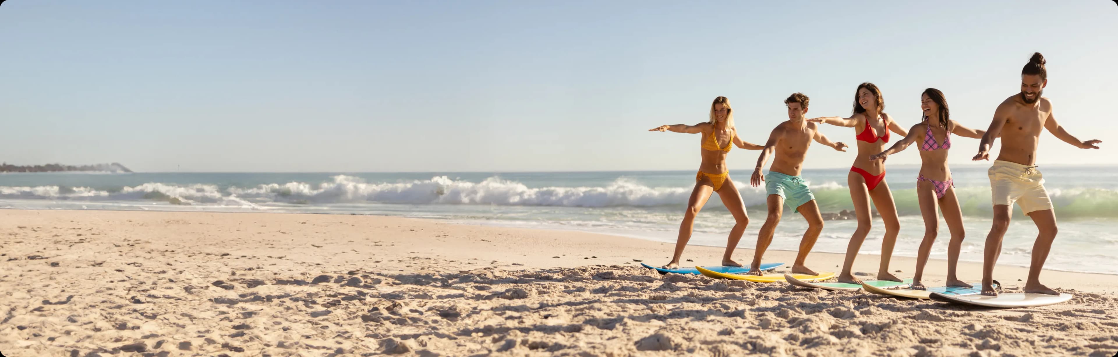 A team of young, sponsored surfers laughing together as they practice balancing on their boards at the shoreline.