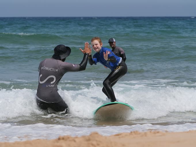 Surf instructor high-fiving a young surf student.